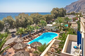 A pool area with lounge chairs and umbrellas, overlooking a beach and the sea.