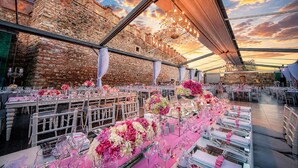 A spacious outdoor dining area with stone walls and a sunset view. Tables are set with pink and white floral centerpieces. - Kalyon Hotel Istanbul (Istanbul)