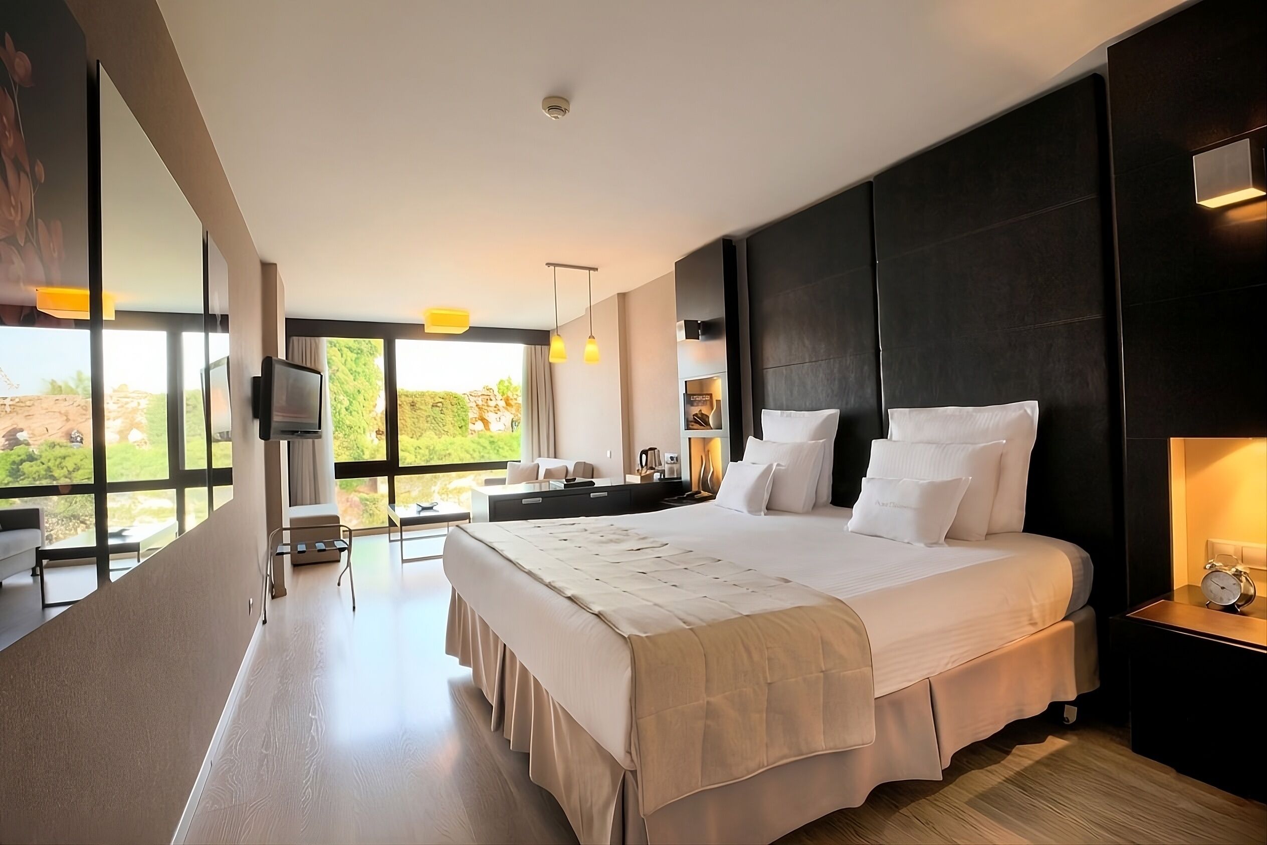Une chambre moderne avec un grand lit, des tables de chevet, un téléviseur et une vue sur l’extérieur.