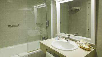 Un baño moderno con ducha de vidrio, bañera y lavamanos con espejo.