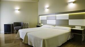 A hotel room with two beds, a chair, a small table, and a wall-mounted light fixture. - Hotel Monarque Torreblanca (Fuengirola)
