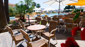 An outdoor seating area with wicker chairs and tables, overlooking a pool and palm trees. - Hotel Monarque Torreblanca (Fuengirola)