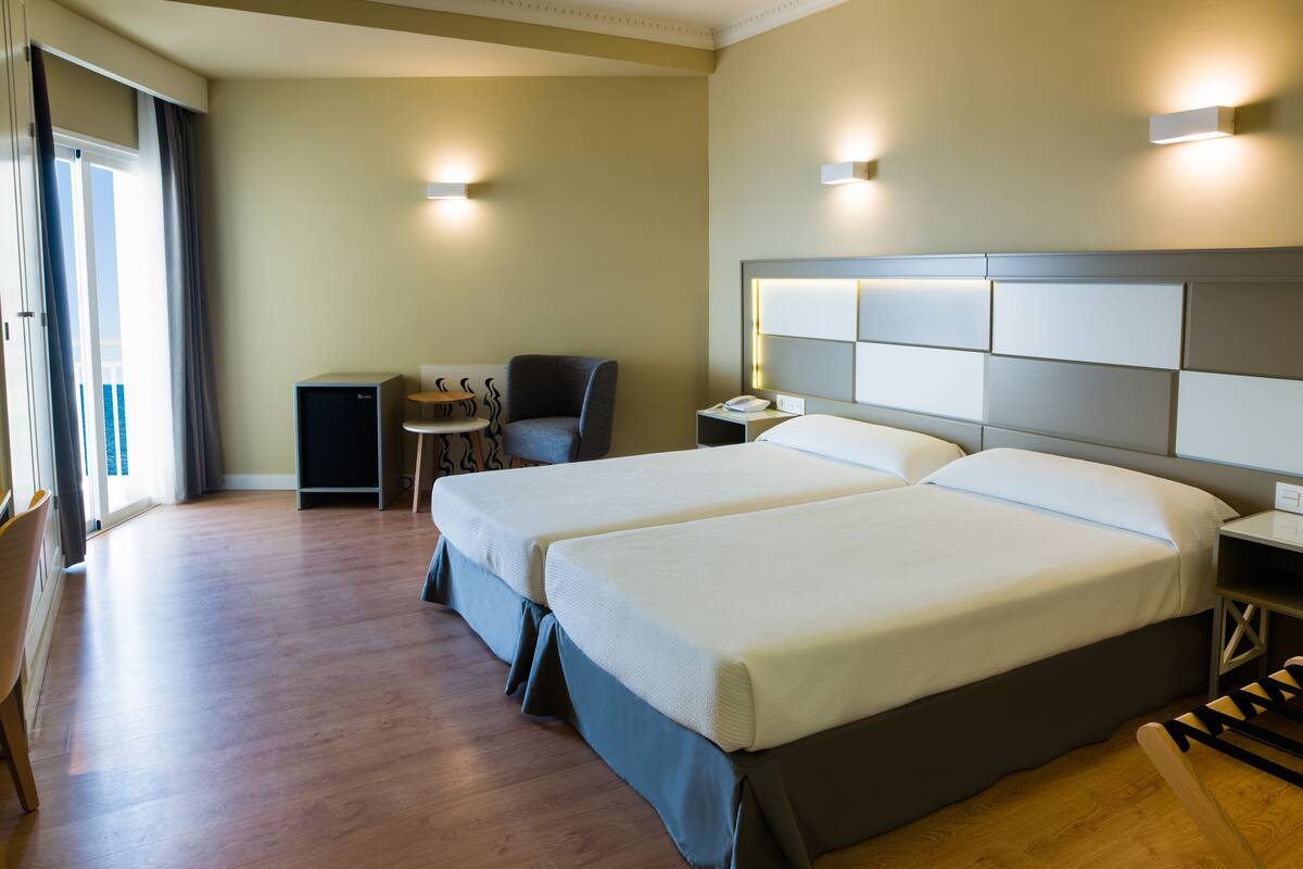 A hotel room with two beds, a desk, a chair, and a small table.