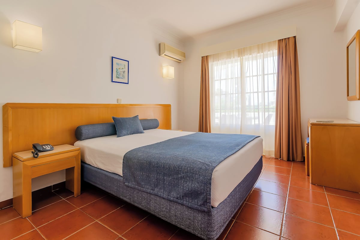 Een hotelkamer met een bed, nachtkastje en een klein bureau.