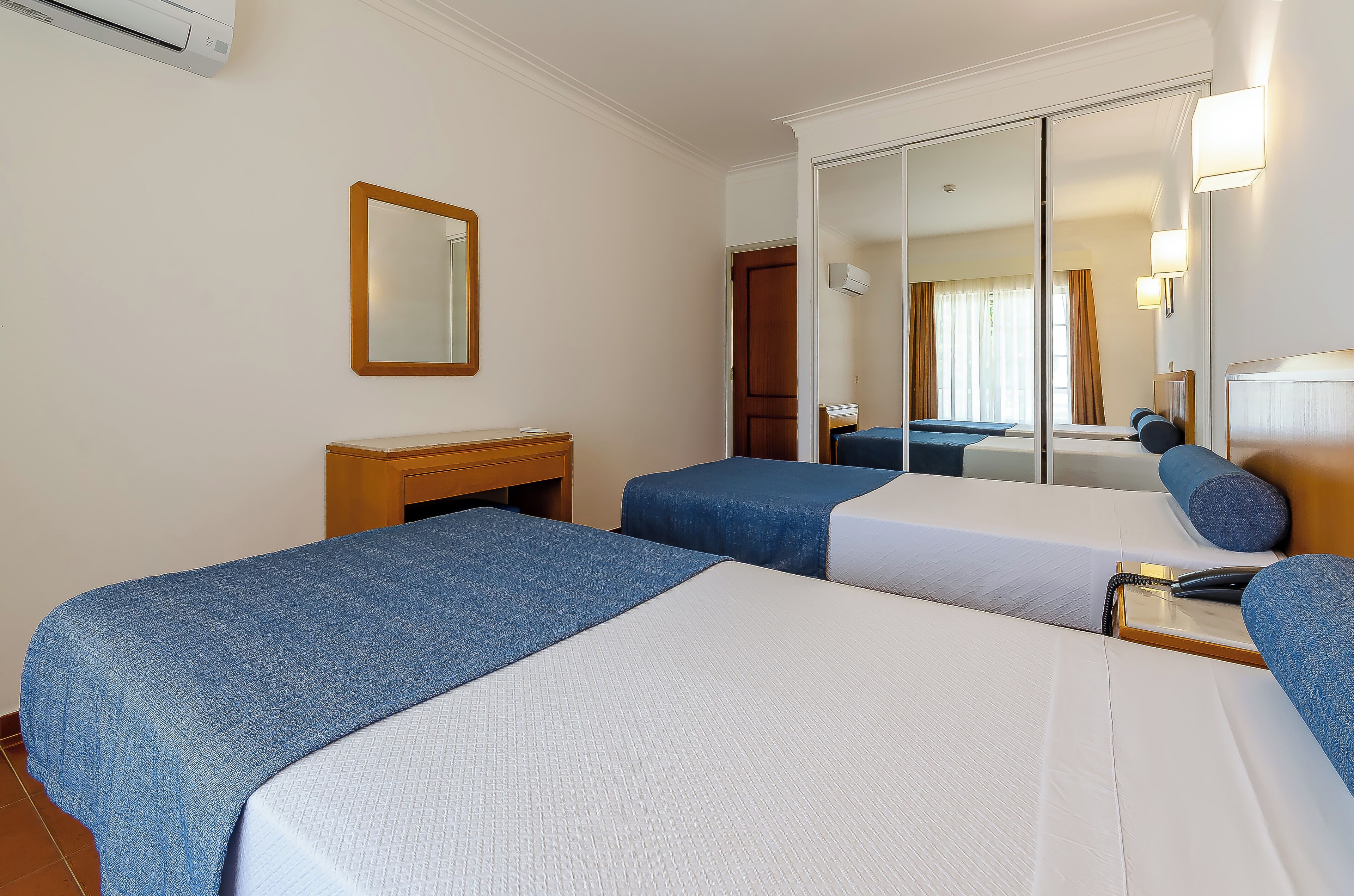 A hotel room with two beds, a bedside table, a mirror, and a wardrobe.