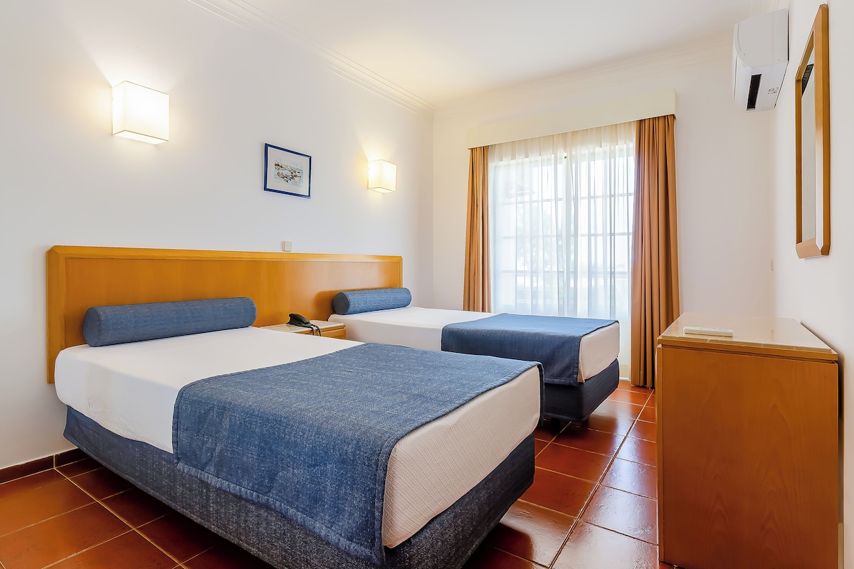 A hotel room with two beds, a desk, and a window with curtains.