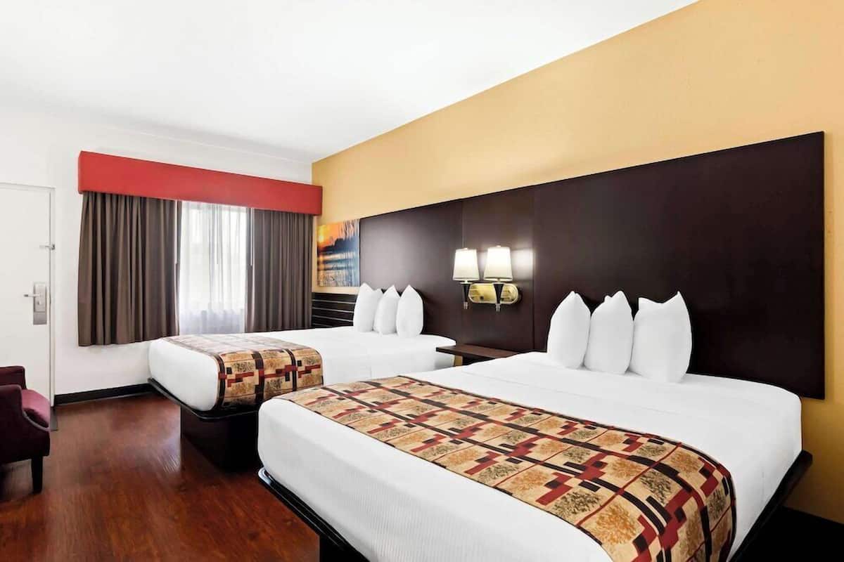 Habitación de hotel con dos camas, una pared de acento roja, un ventanal con cortinas y una lámpara de pared.