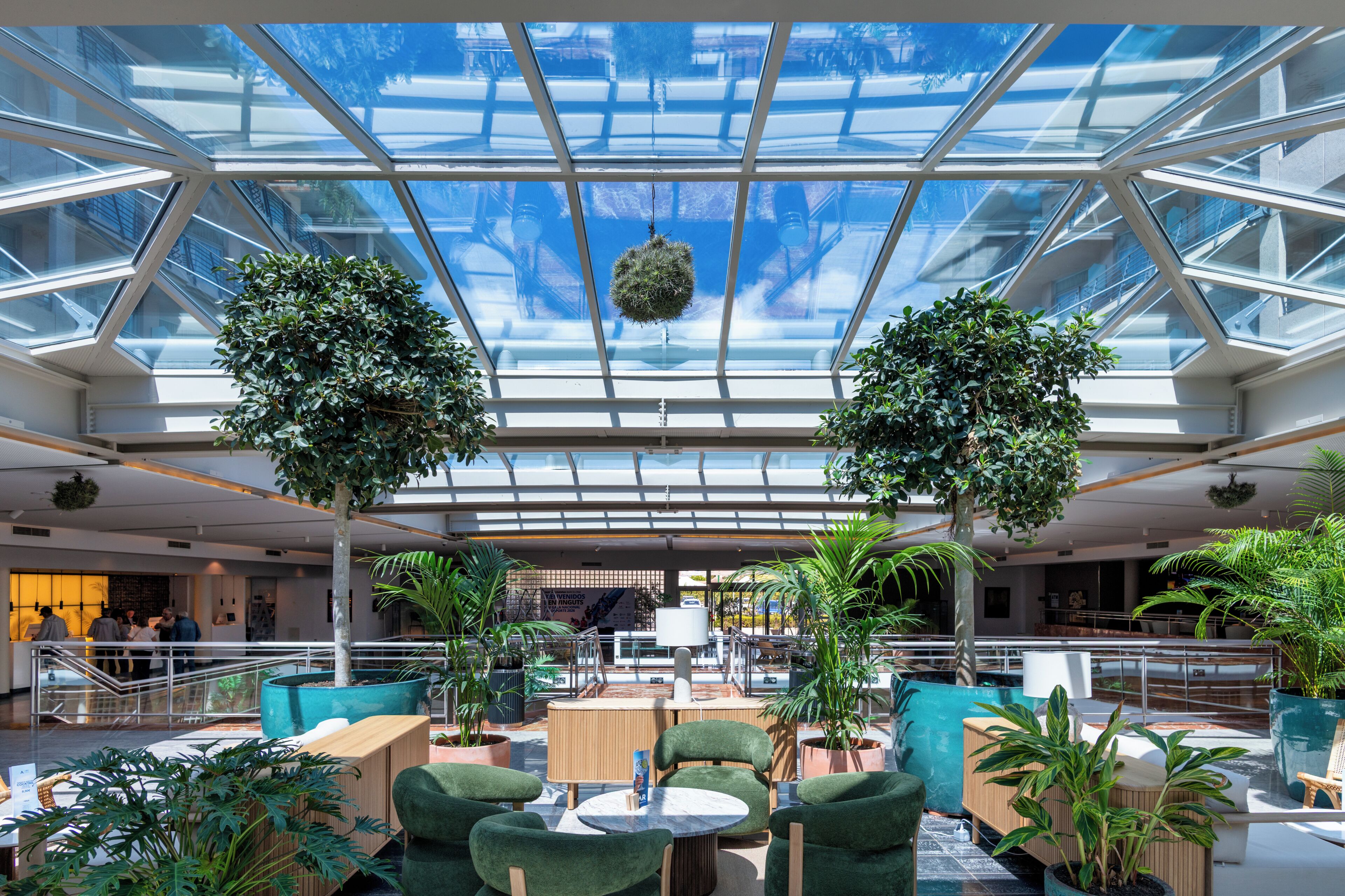 A spacious atrium with a glass ceiling, seating areas, and potted plants.
