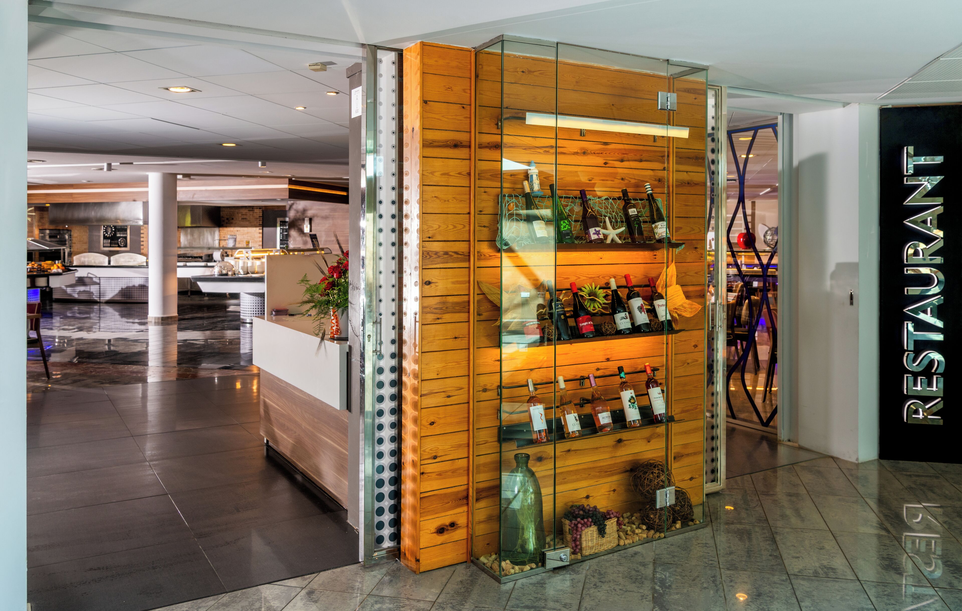 A modern restaurant with a wooden interior, a wine display, and a view of the kitchen area.