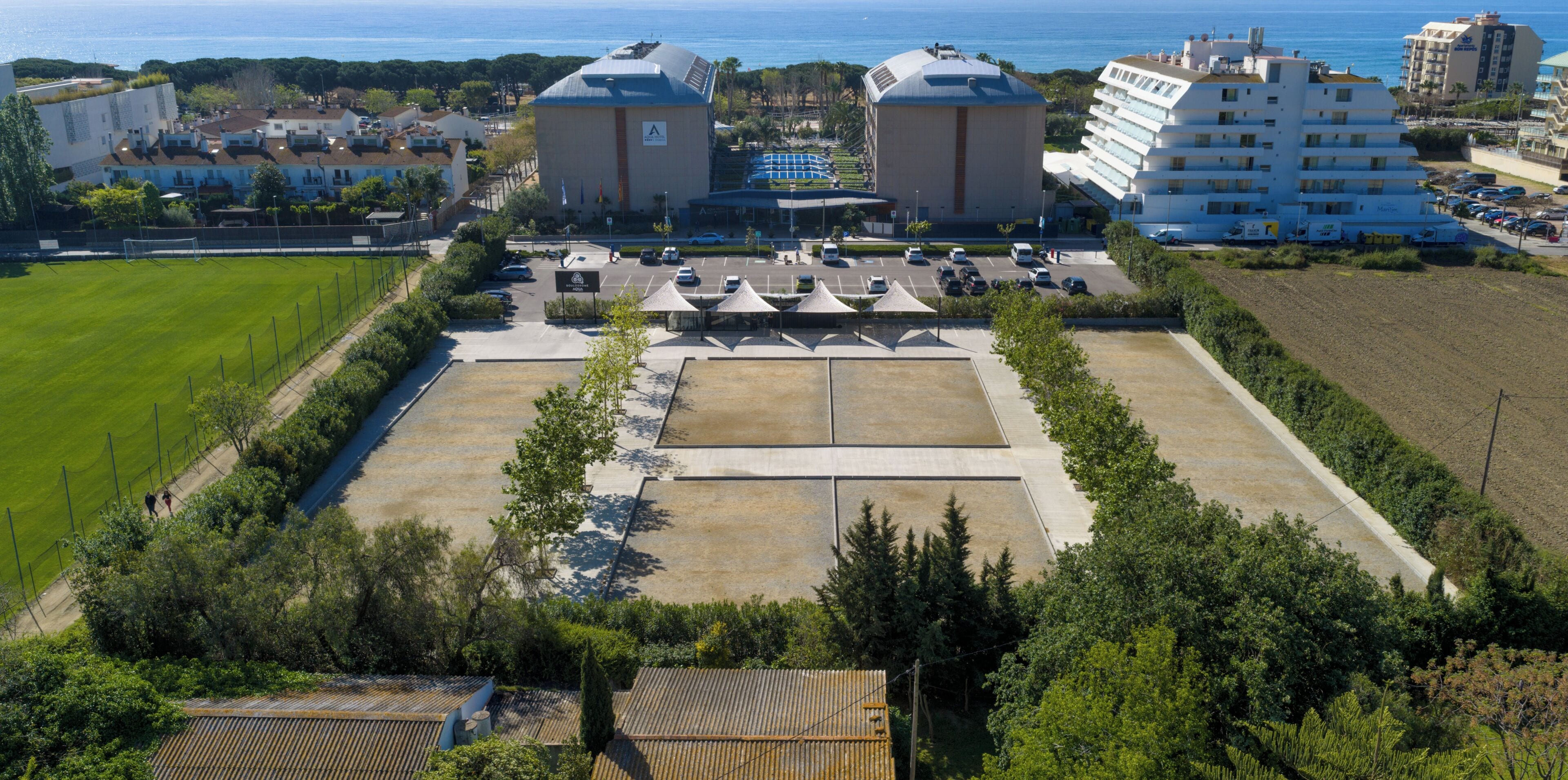 Vista aérea de un hotel con un amplio estacionamiento, dos edificios destacados con cúpulas y una vista al mar en el fondo.