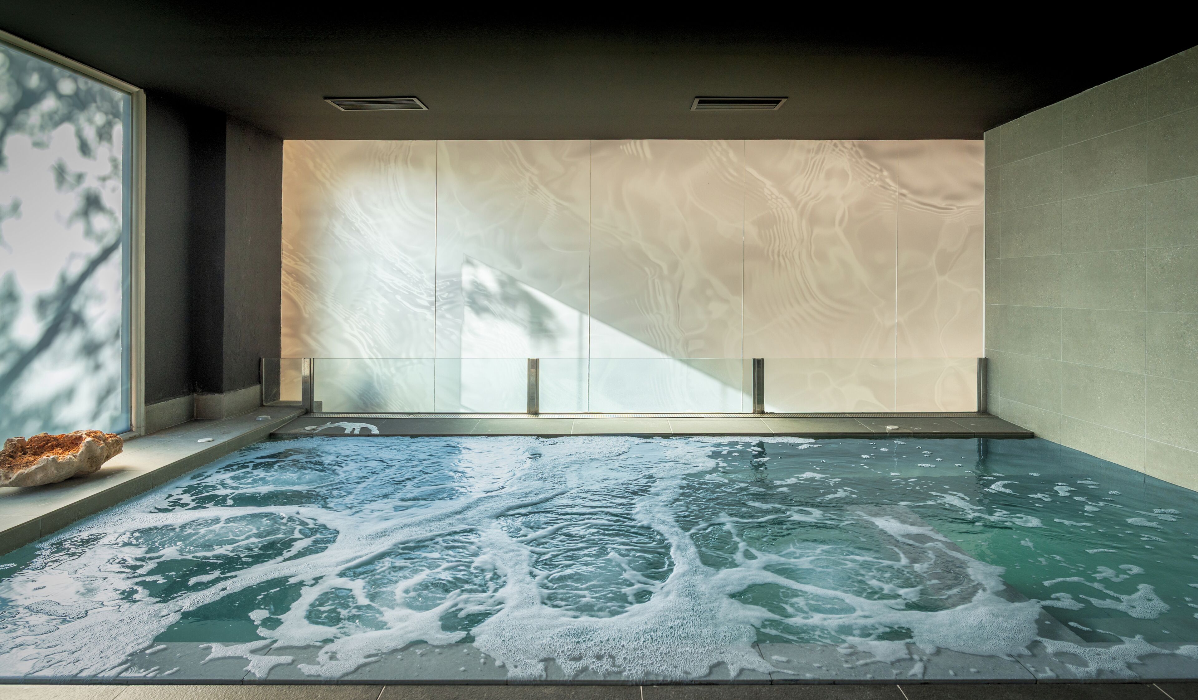 Un cuarto de spa con una bañera grande, un separador de vidrio y detalles de piedra.
