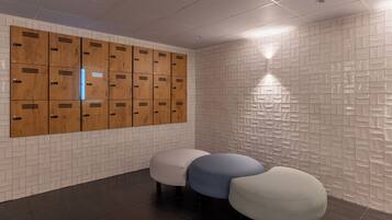 A locker room with wooden lockers, a white tiled wall, and three ottomans.