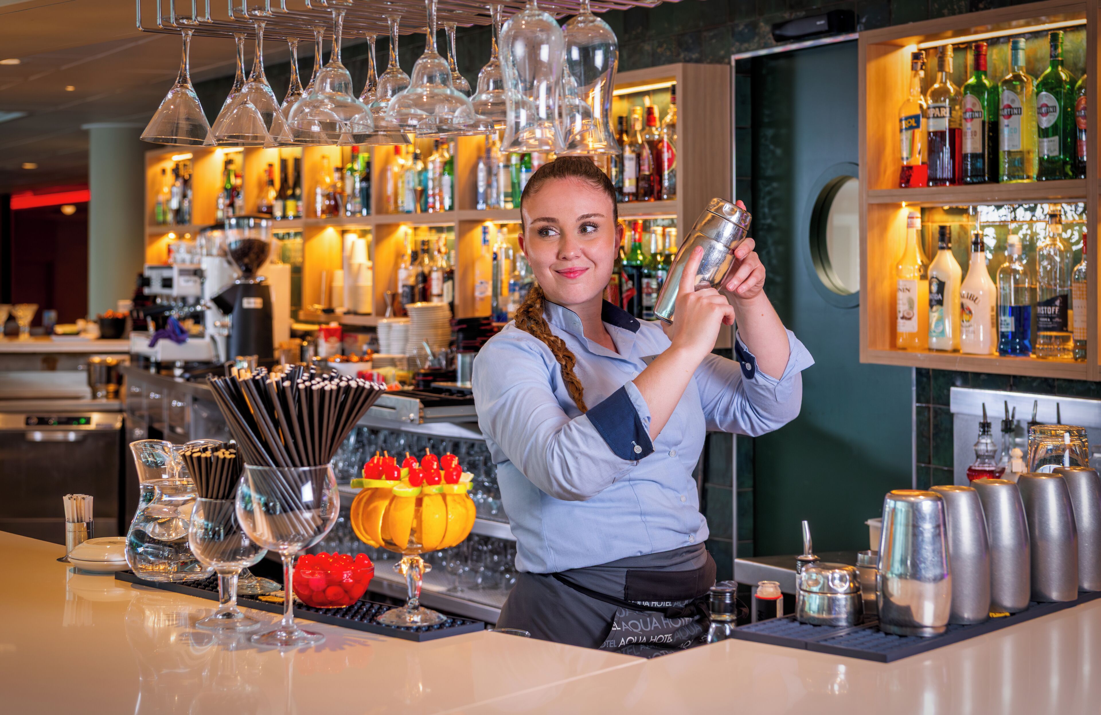 Eine Bar mit Bartender, einer Theke, Gläsern, Flaschen und einer dekorativen Obstschale.