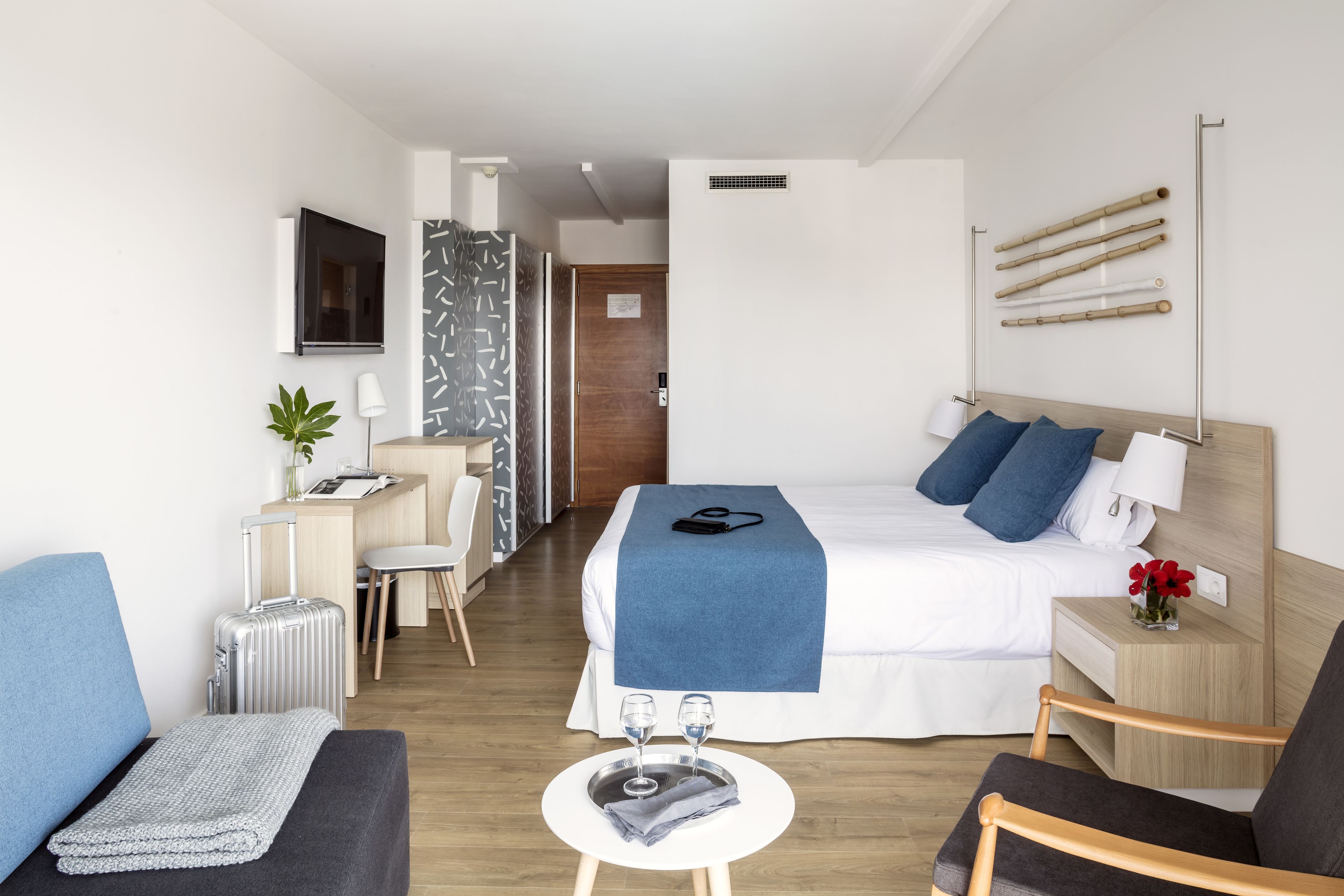 Una habitación de hotel moderna con cama, mesita de noche, silla, escritorio y una pequeña zona de estar.