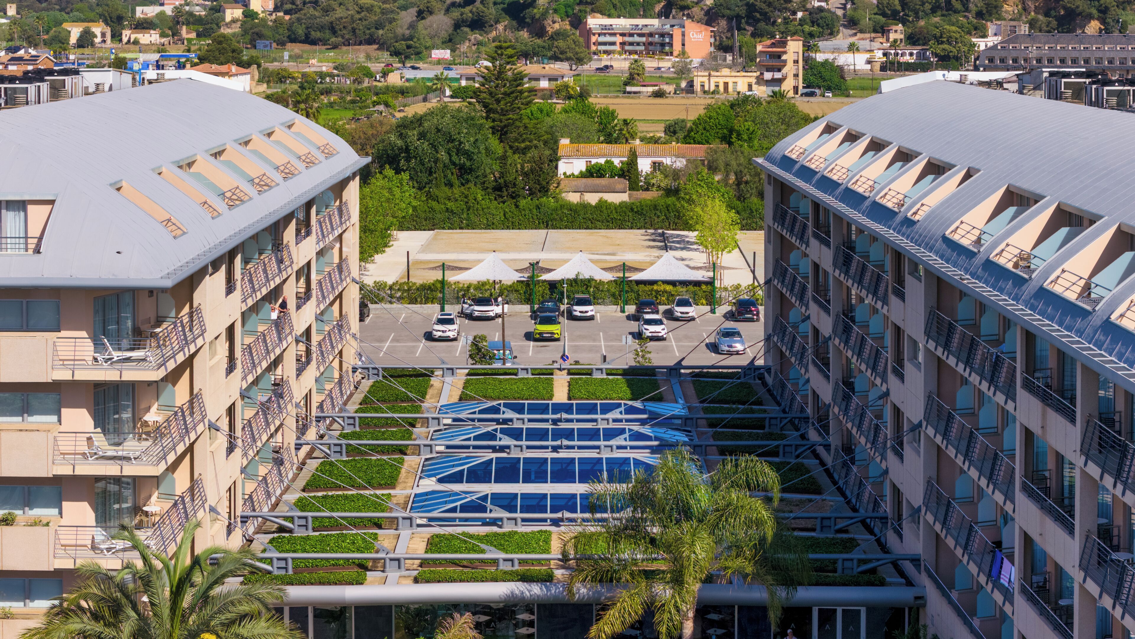 A multi-story hotel with a rooftop parking area, a central courtyard with greenery, and a view of the surrounding neighborhood.