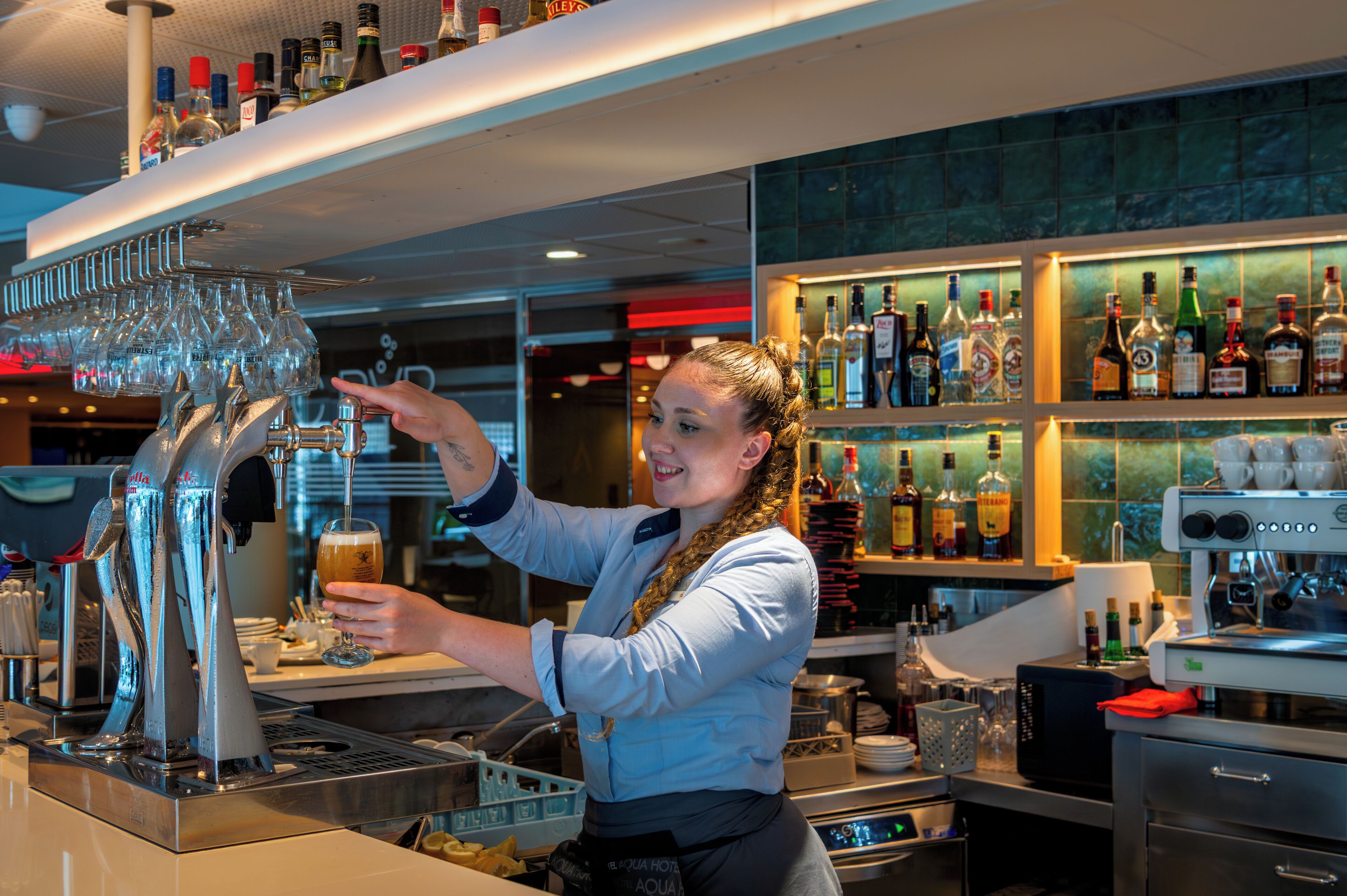 Un espace bar avec un barman, un réfrigérateur à vin et un assortiment de bouteilles d’alcool.