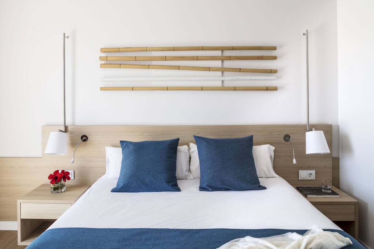 Una cama bien hecha con almohadas azules, un cabecero de madera y lámparas de noche.
