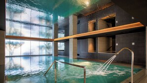 Una piscina interior con agua cristalina, una barandilla de metal y vistas al exterior a través de amplias ventanas.