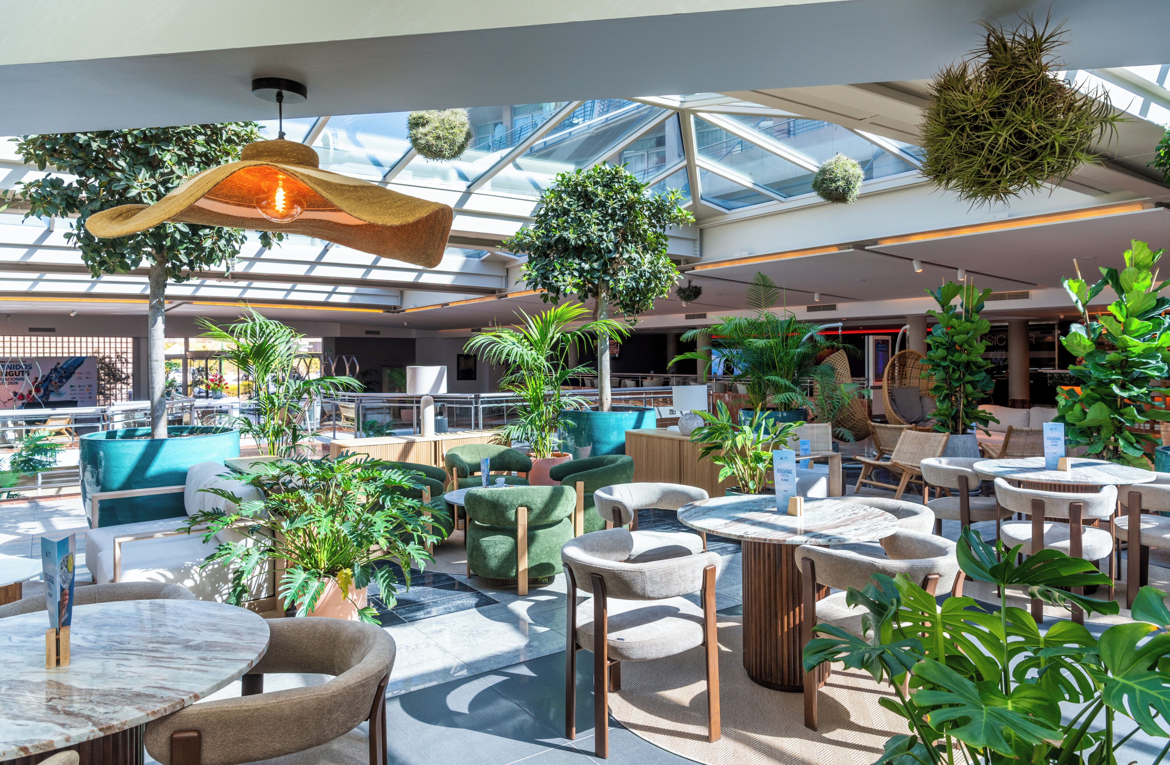 A spacious indoor area with multiple seating arrangements, including tables and chairs, surrounded by various potted plants and greenery.
