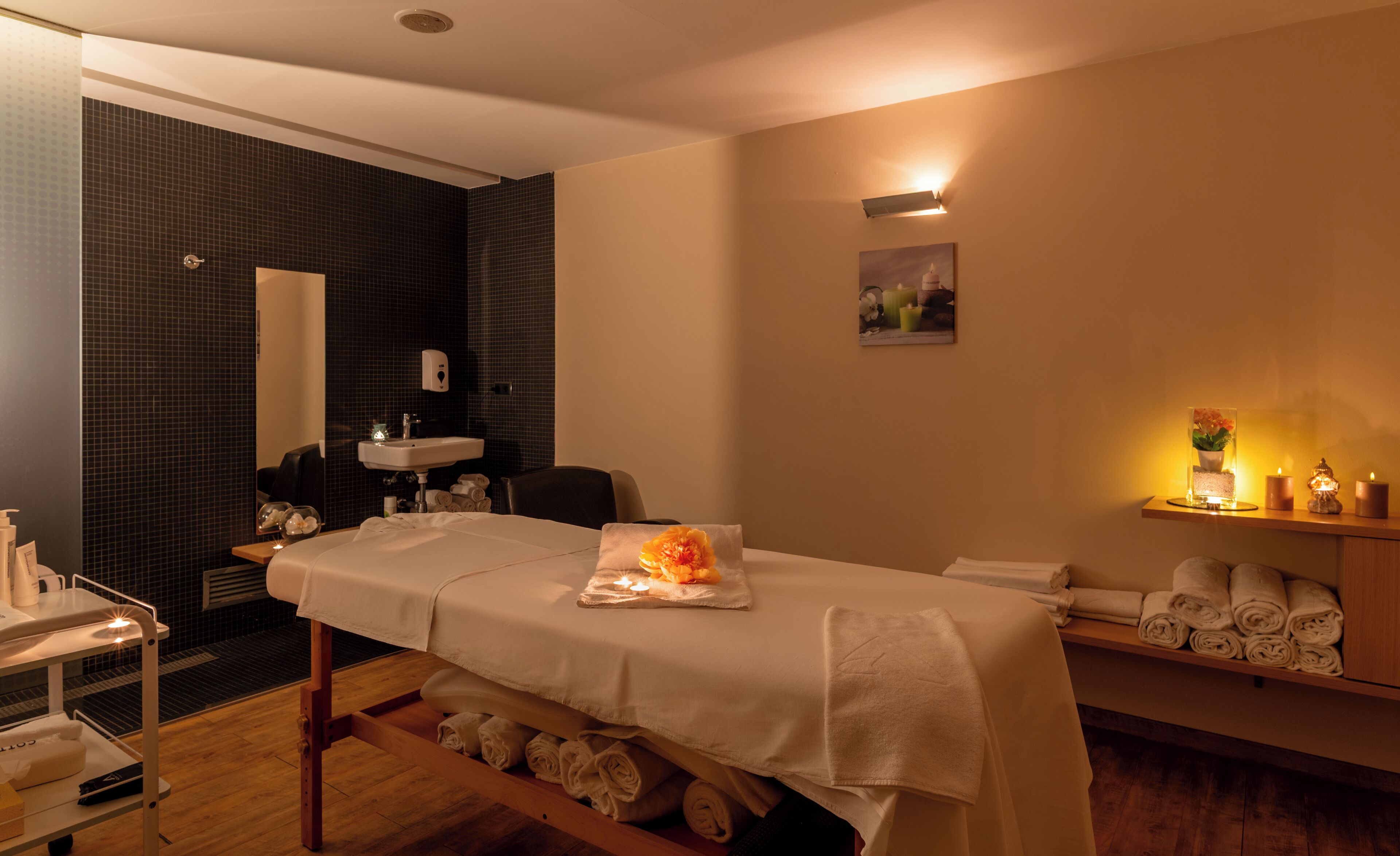A spa room with a massage table, a sink, a mirror, and a shelf with towels.