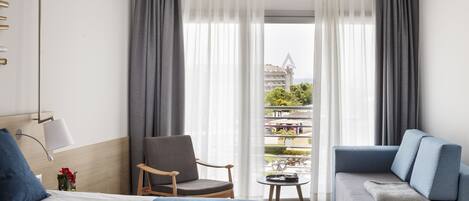 Habitación de hotel con cama, sofá, una silla, una mesita y balcón con vistas.