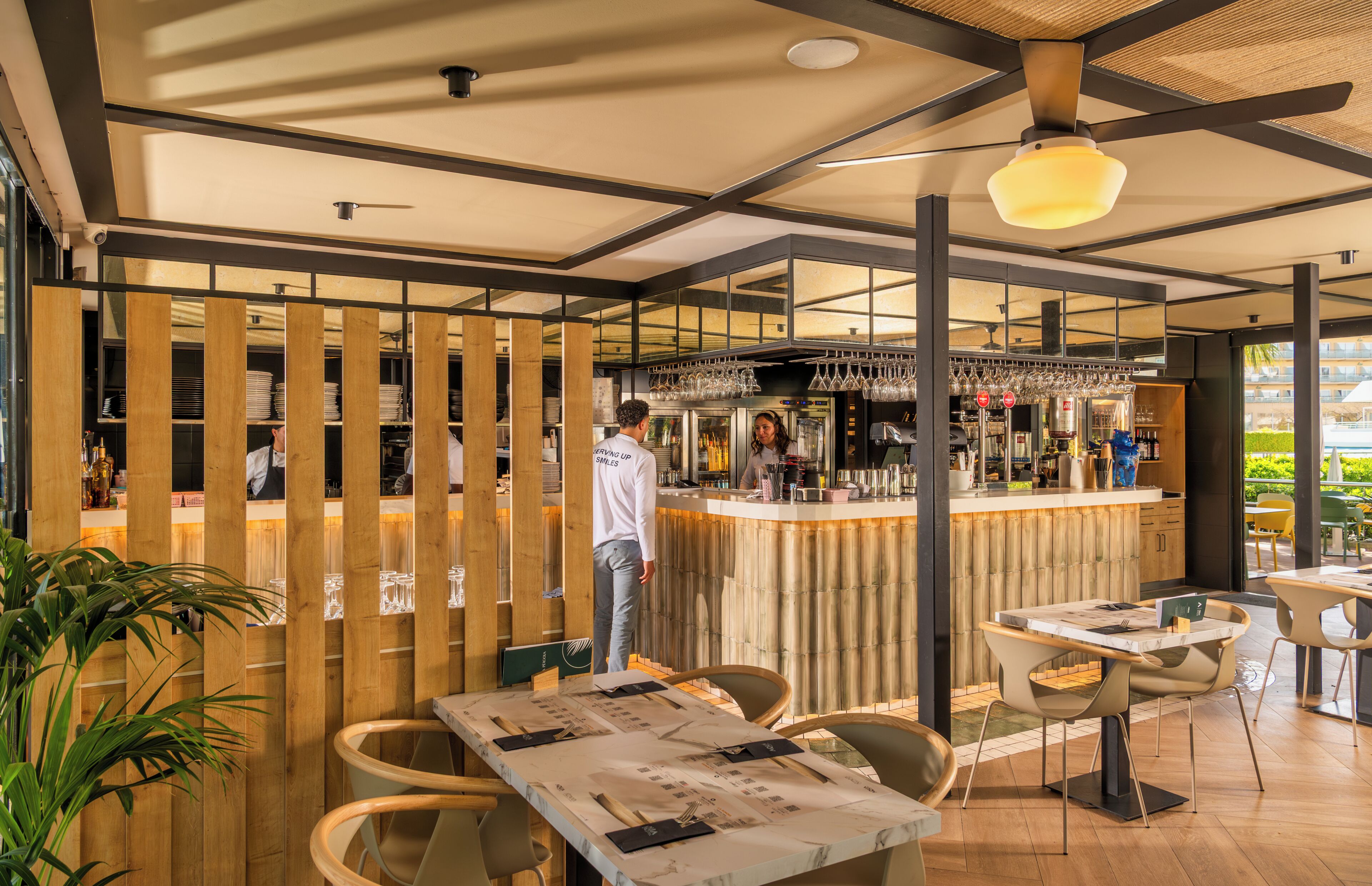 Un restaurante con zona de bar, separadores de madera y mesas con menús.