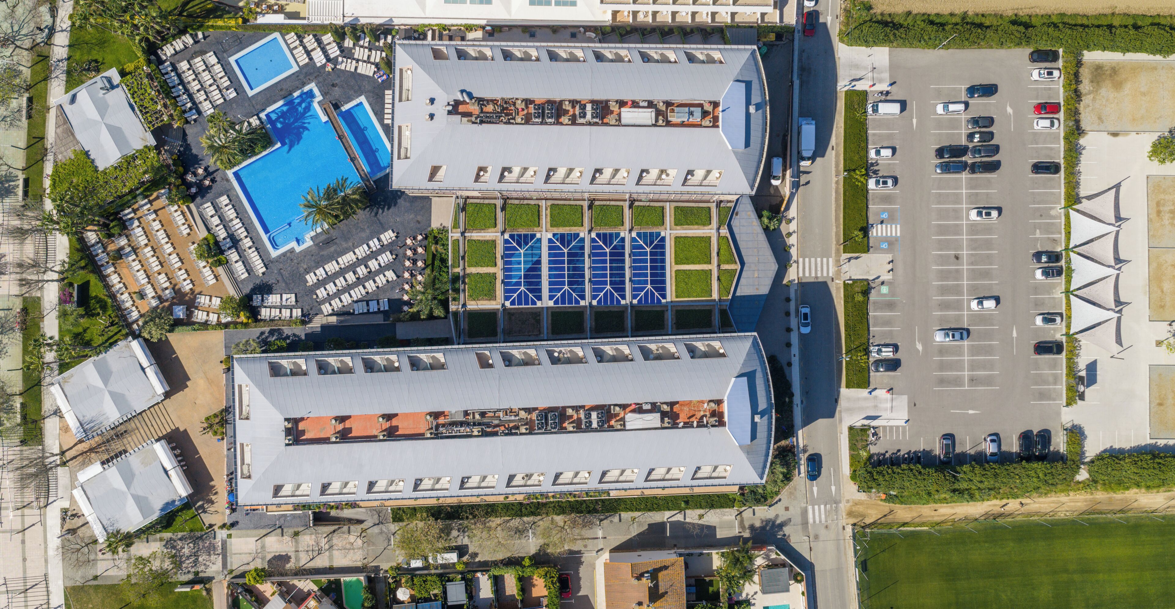 Vista aérea de un hotel con piscina, varios estacionamientos y un edificio grande con techo plano.
