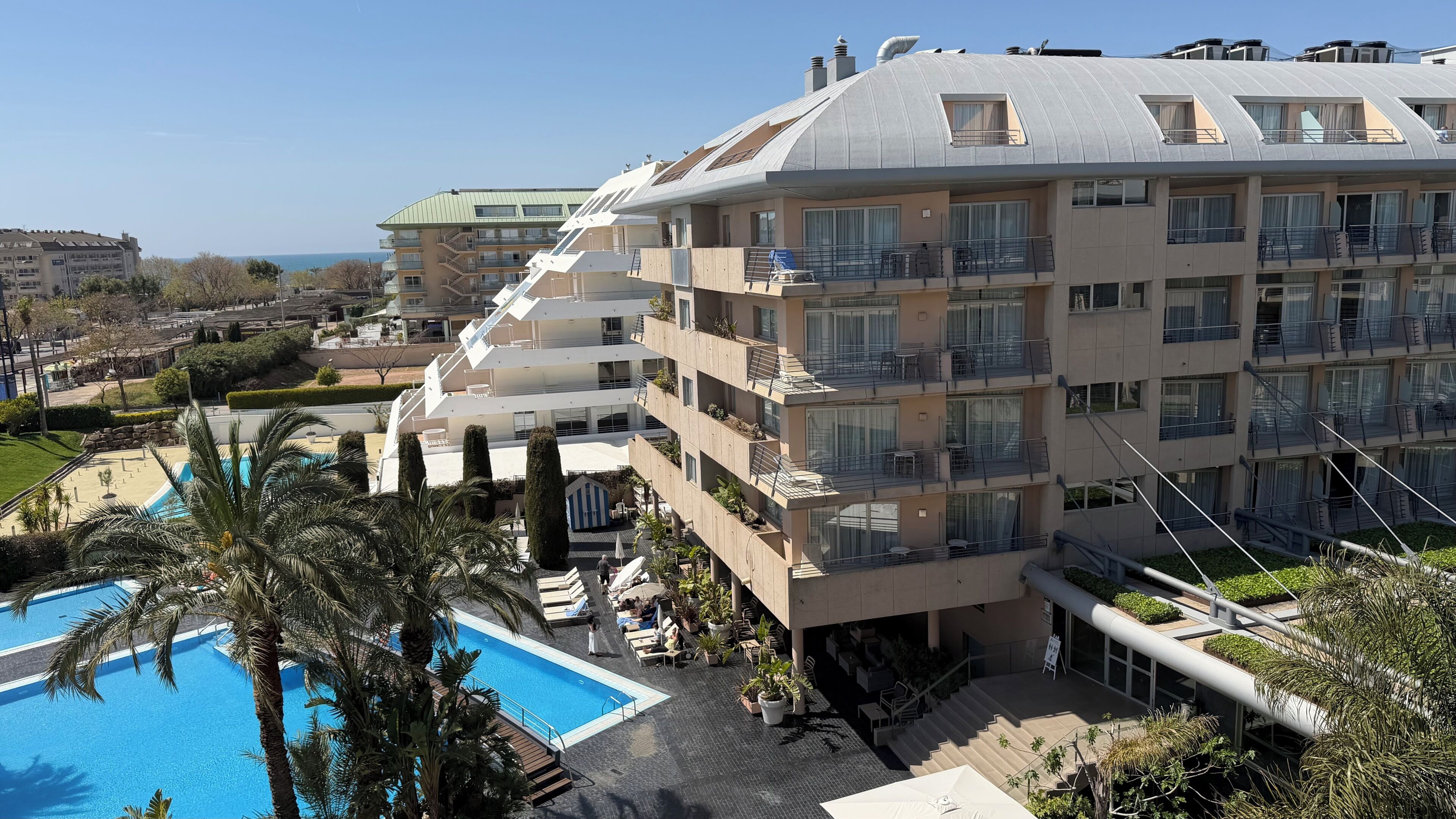 Ein mehrstöckiges Hotel mit Balkonen, einem Schwimmbad und Meerblick.