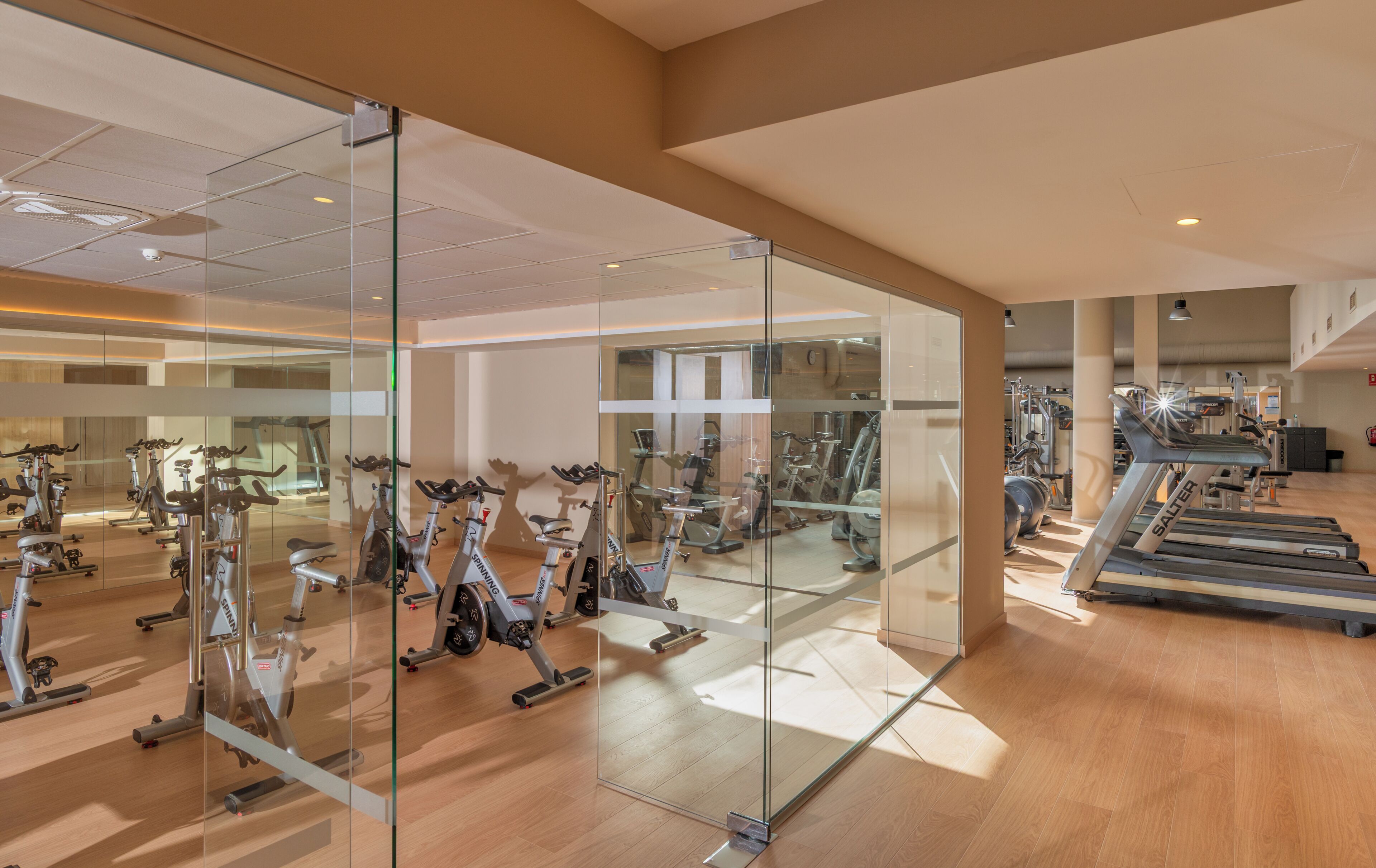 A gym with exercise equipment, a mirrored wall, and a wooden floor.