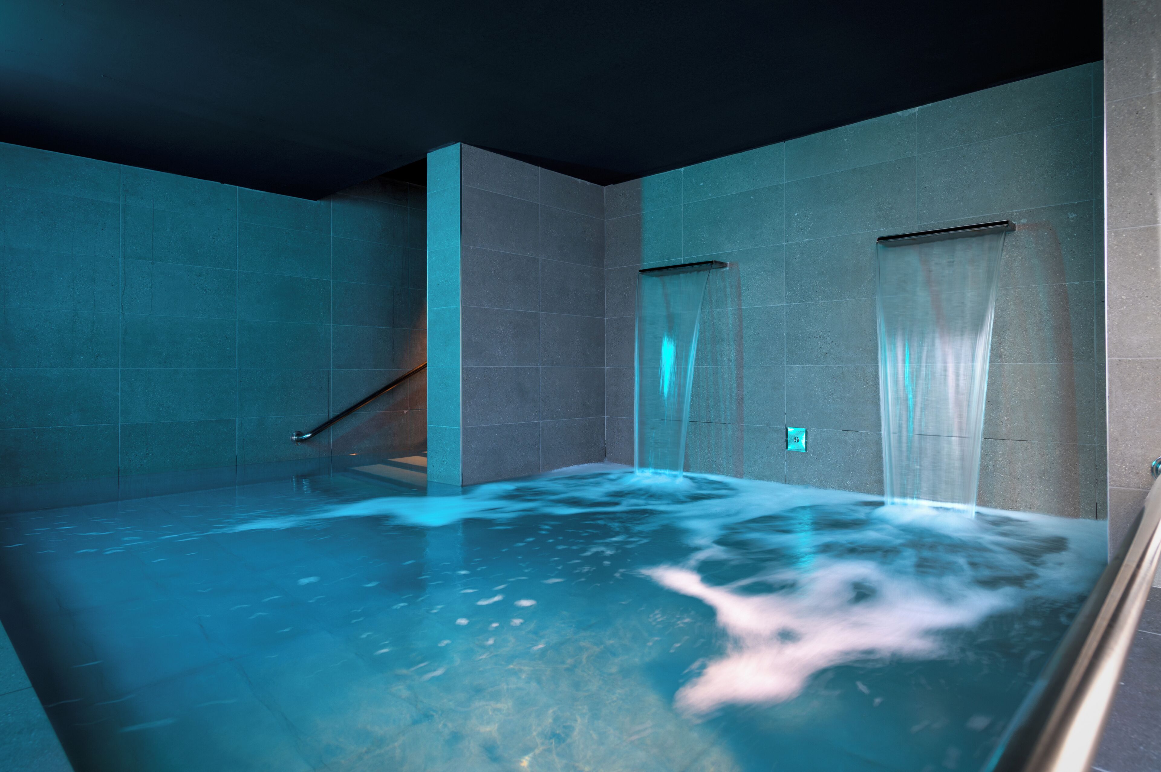 Un moderno cuarto de spa con un amplio jacuzzi, paredes con azulejos y un separador de vidrio.