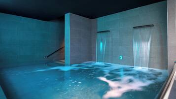 Un moderno cuarto de spa con un amplio jacuzzi, paredes con azulejos y un separador de vidrio.