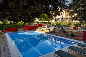 A swimming pool with lounge chairs and a red wall. - AQUA Hotel Bertran Park (Lloret de Mar)