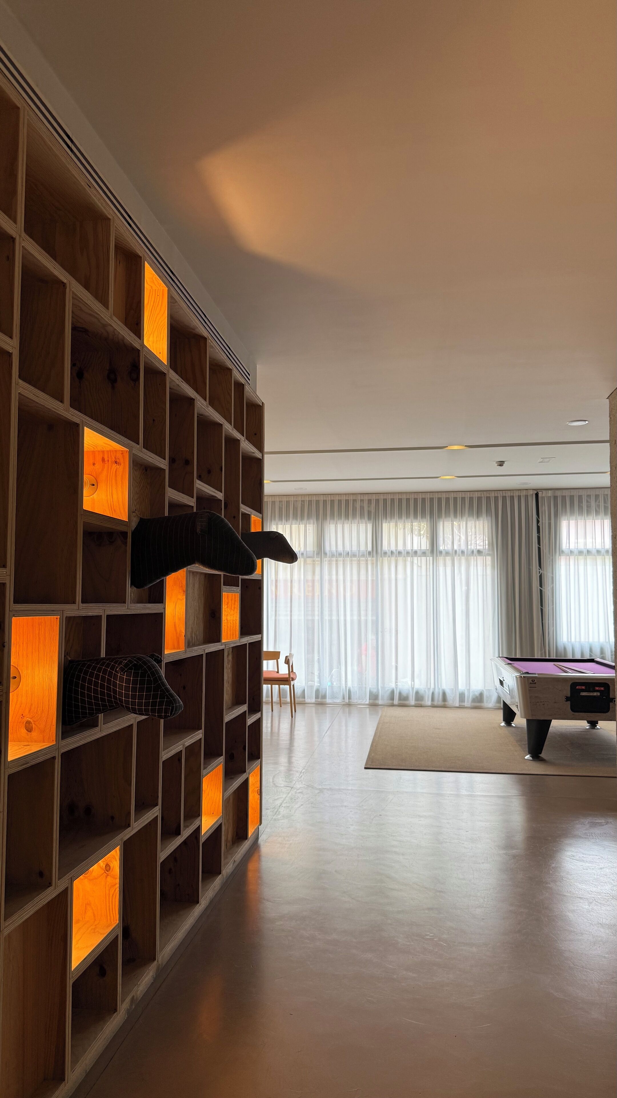 Un salon moderne avec une bibliothèque en bois, une table de billard et un fauteuil.