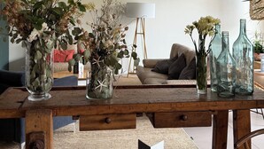 A cozy living room with a wooden coffee table, a round dining table, and a sofa. There are decorative vases with flowers and empty glass bottles on the coffee table. - AQUA Hotel Bertran Park (Lloret de Mar)