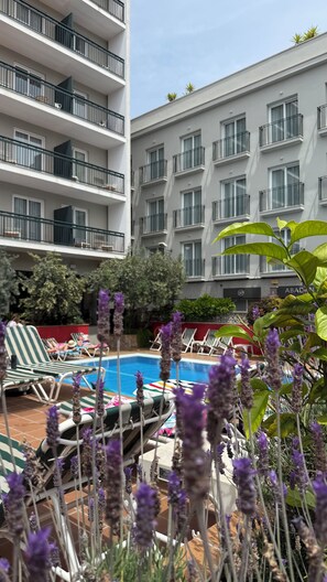 A pool area with lounge chairs, a swimming pool, and a building with multiple balconies. - AQUA Hotel Bertran Park (Lloret de Mar)