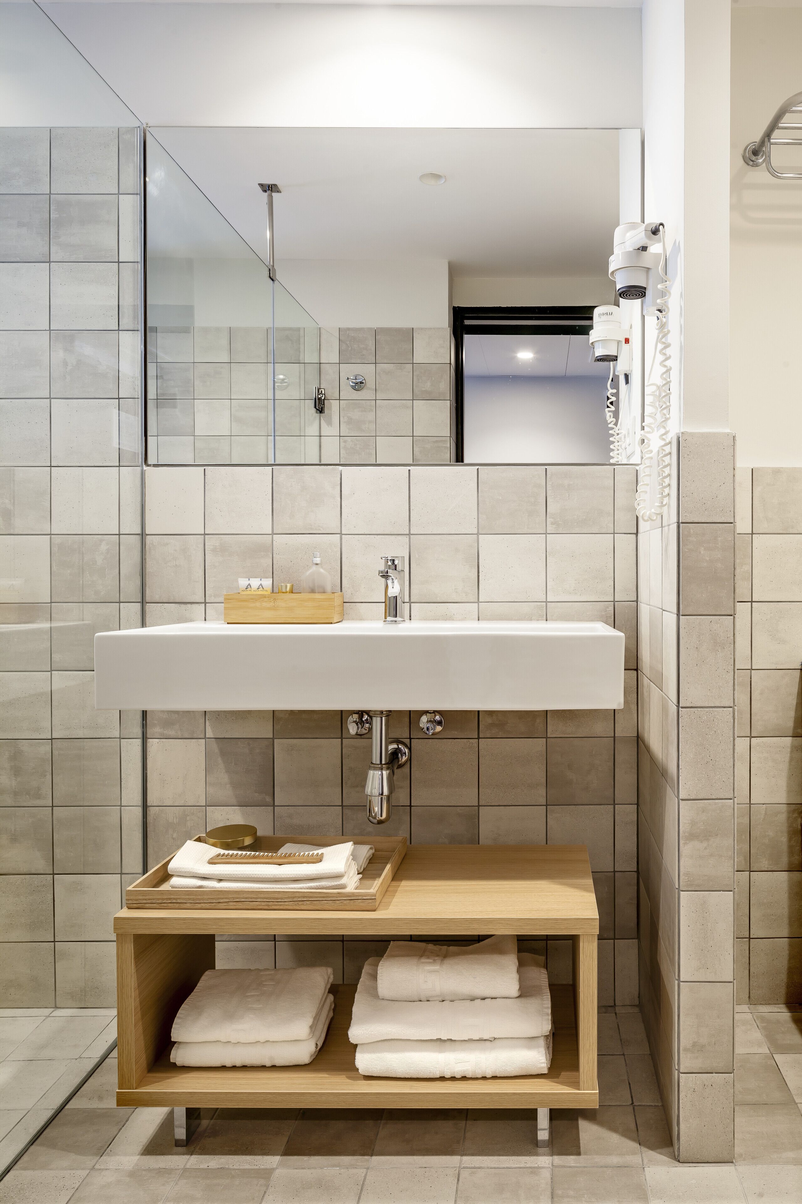 A modern bathroom with a large sink, a glass shower enclosure, and a wooden shelf with towels.