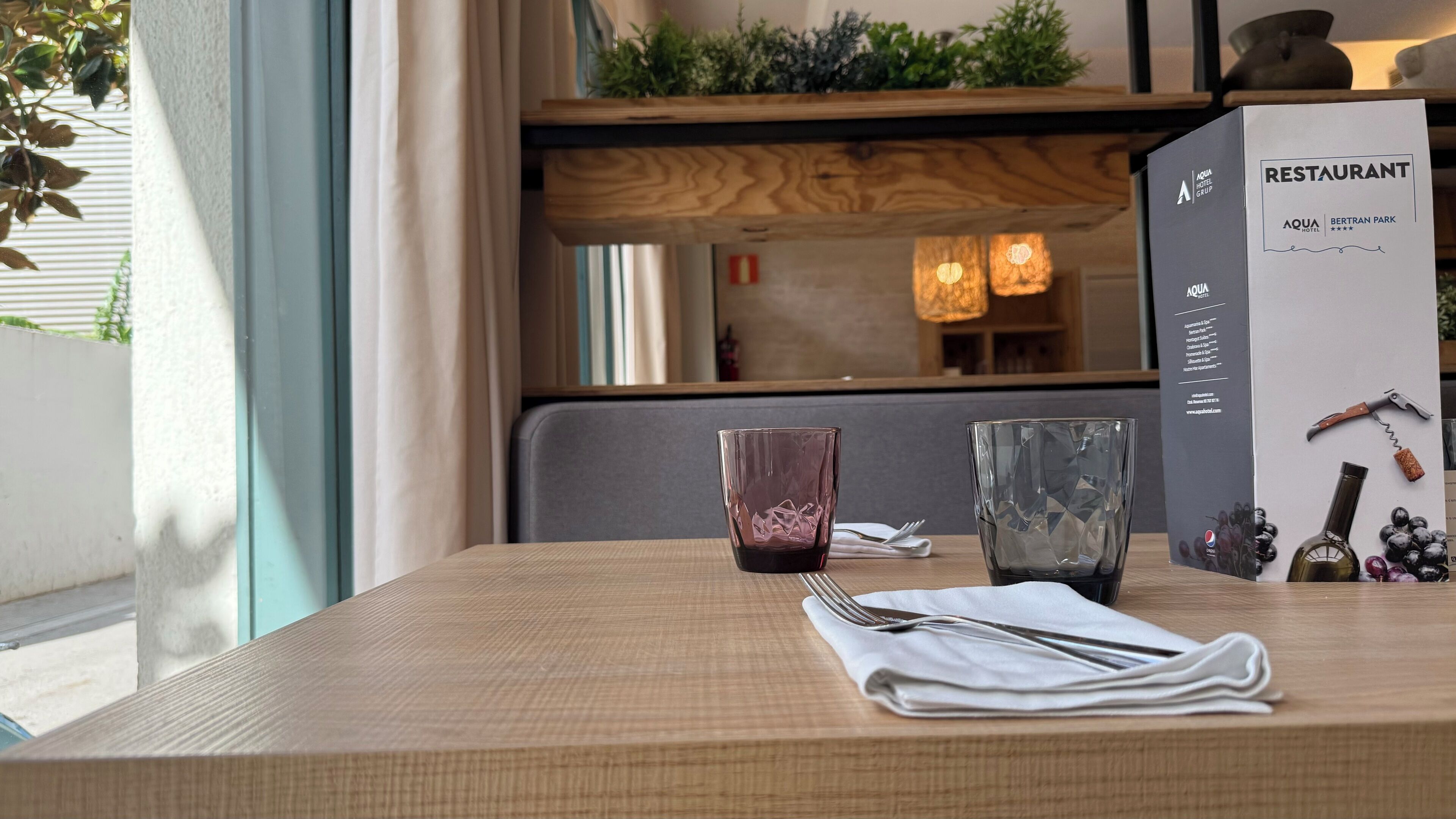 A table with a menu box, two glasses, and cutlery.