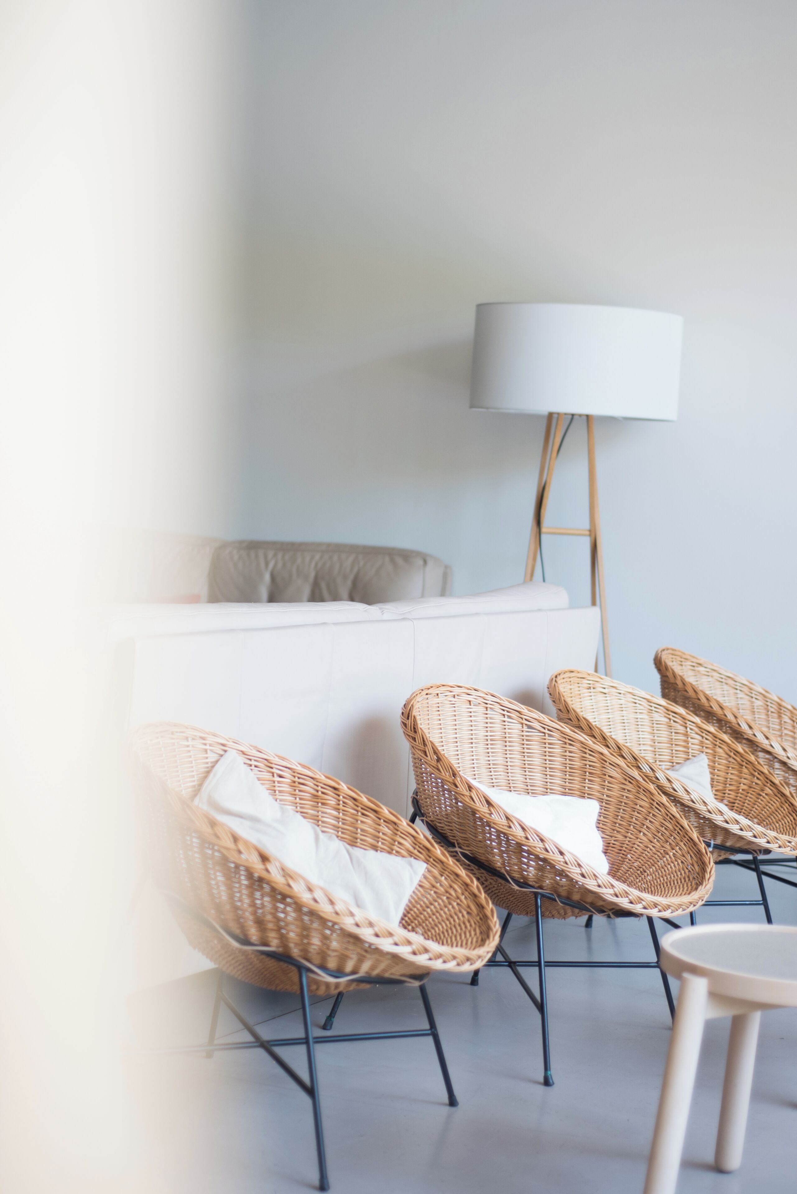 Una habitación con un sofá blanco, dos sillas de mimbre con cojines, una mesita redonda y una lámpara de pie.
