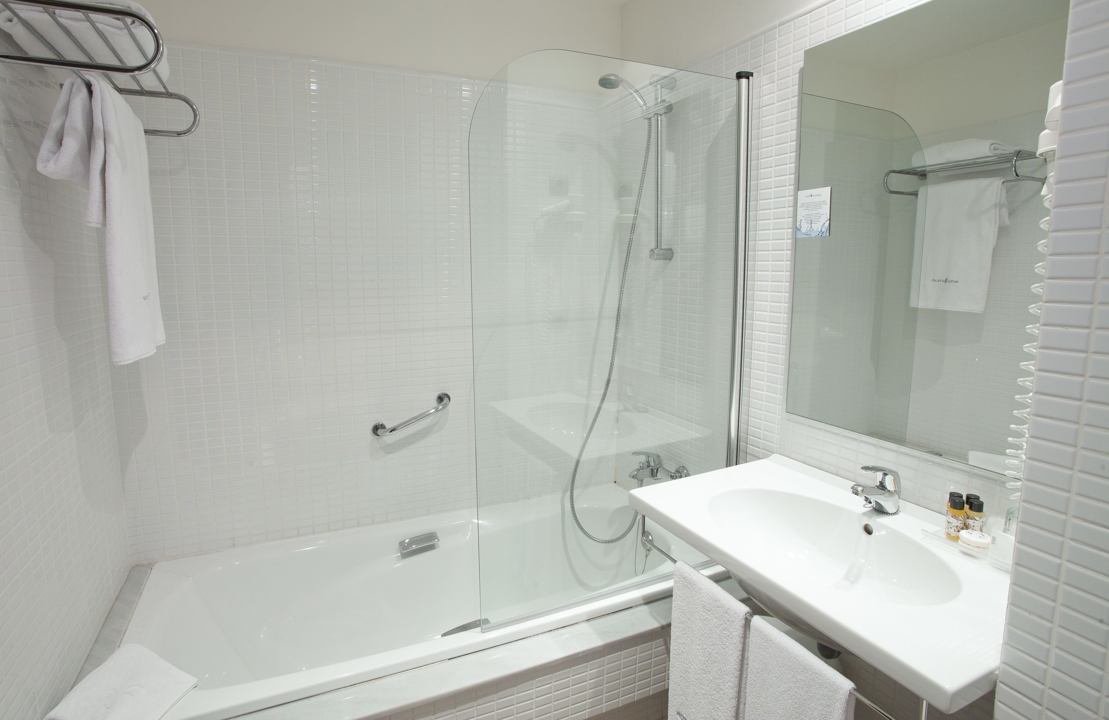 A modern bathroom with a glass-enclosed shower, a white bathtub, and a sink with a mirror above it.