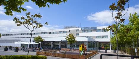A modern building with a playground area in front, outdoor seating, and a clear sky.