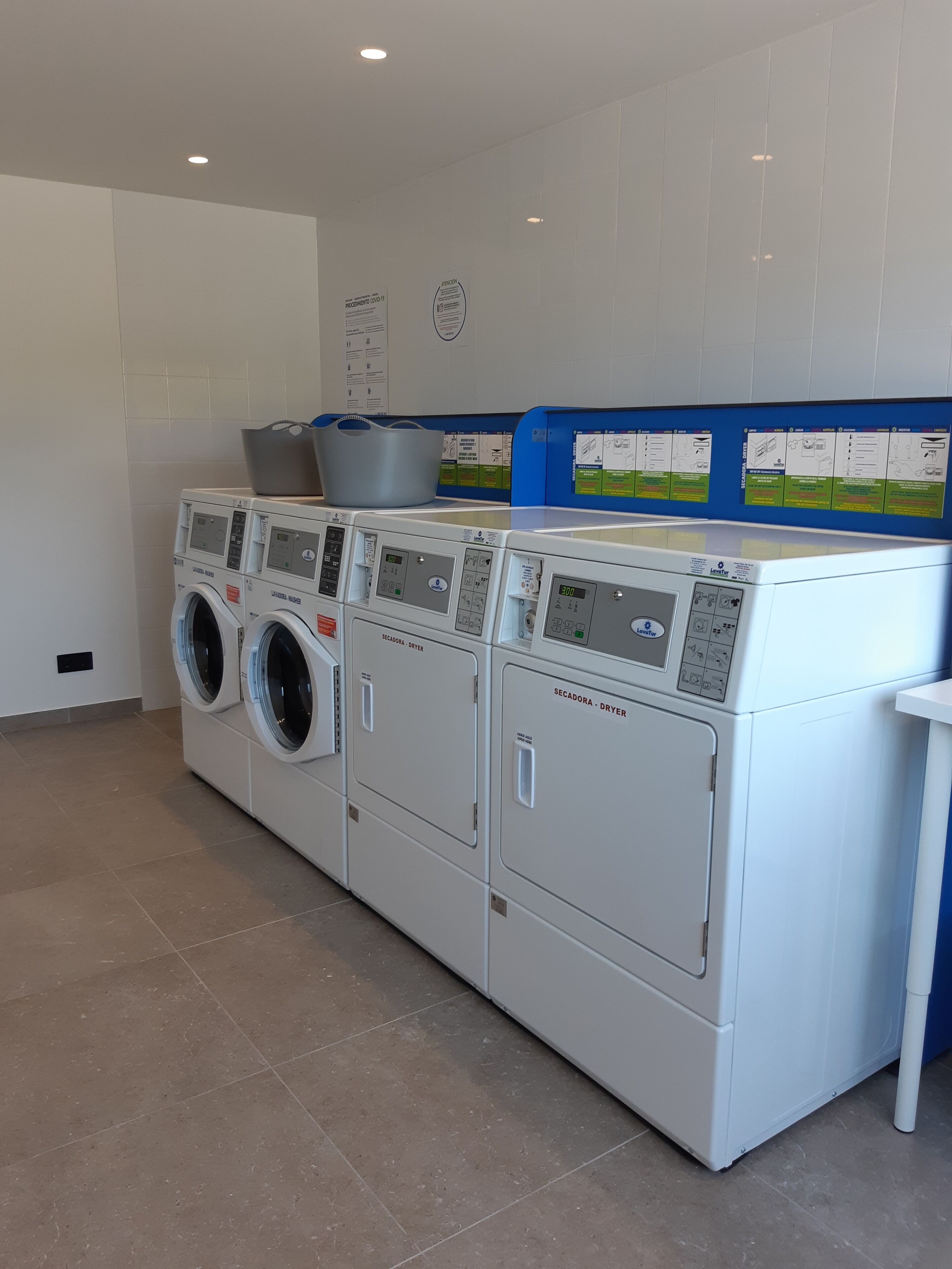 A row of front-loading washing machines with a blue informational board above them.
