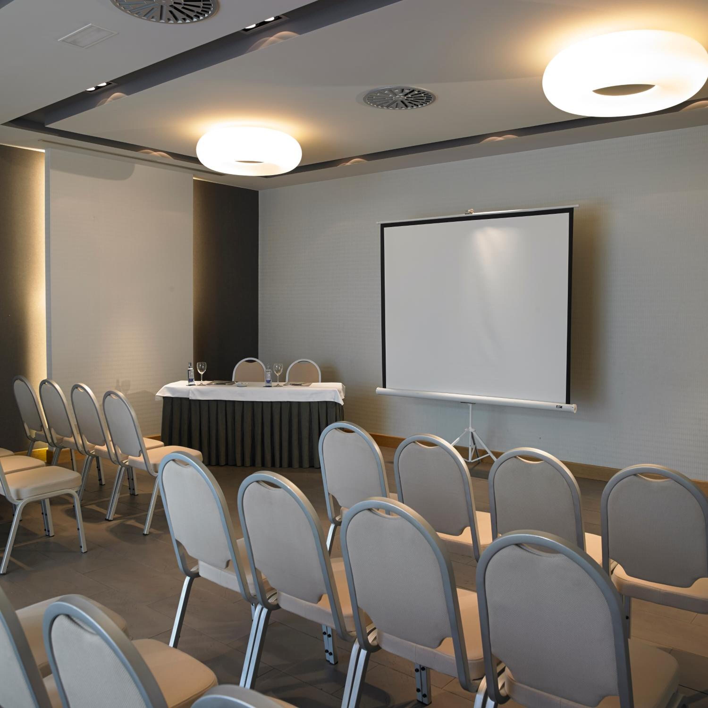A conference room with a whiteboard, a projector screen, and rows of chairs.
