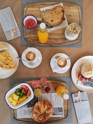 A breakfast setting with a variety of food items including toast, croissants, fruit, and beverages on a wooden board. - Aparthotel Attica21 As Galeras (Oleiros)
