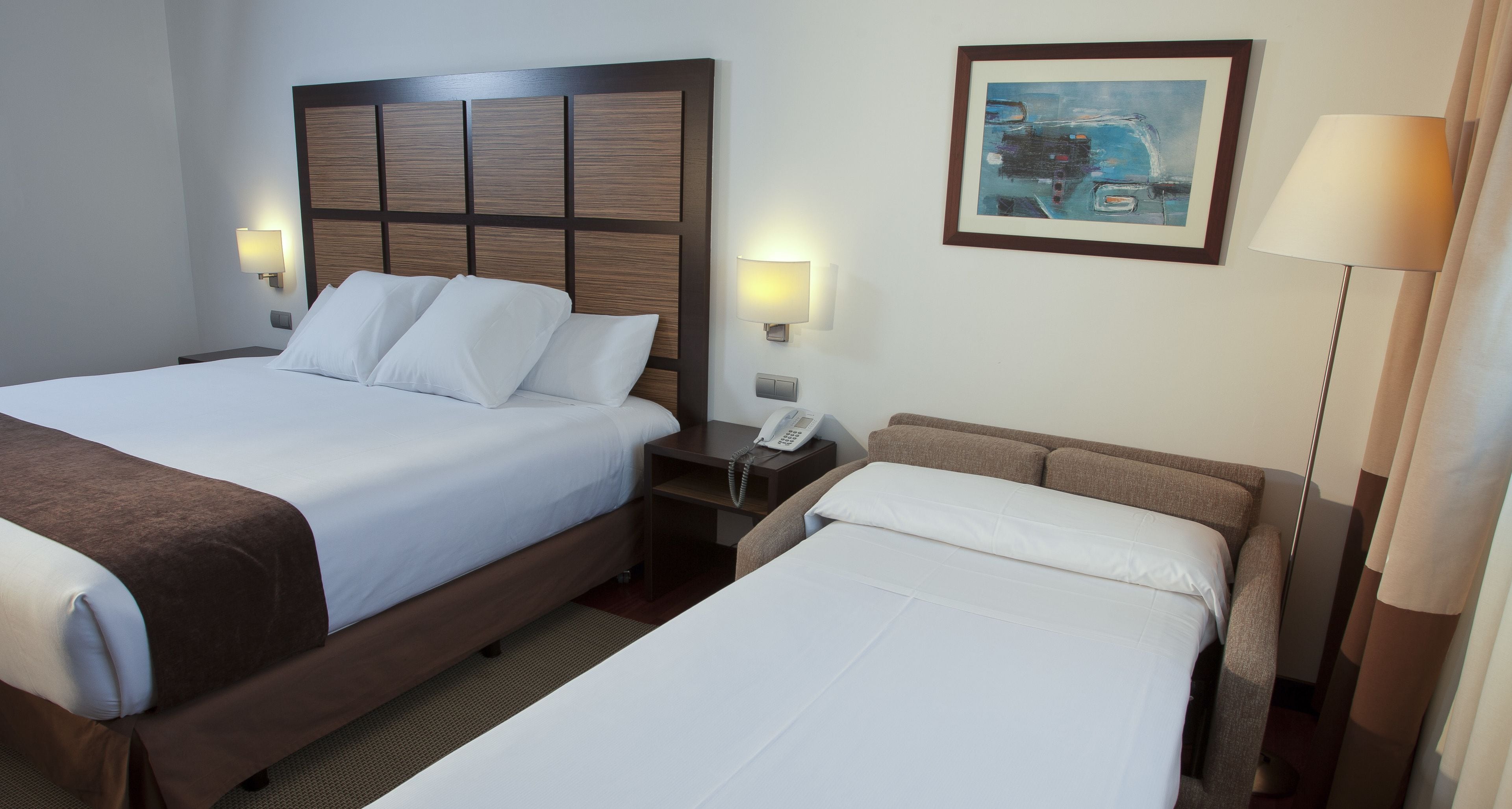 Ein Hotelzimmer mit zwei Betten, einem Nachttisch mit Telefon und einem Bild an der Wand.