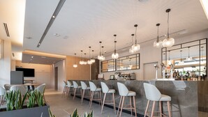 Un área de bar moderna con una barra alargada, varios taburetes y luces colgantes.