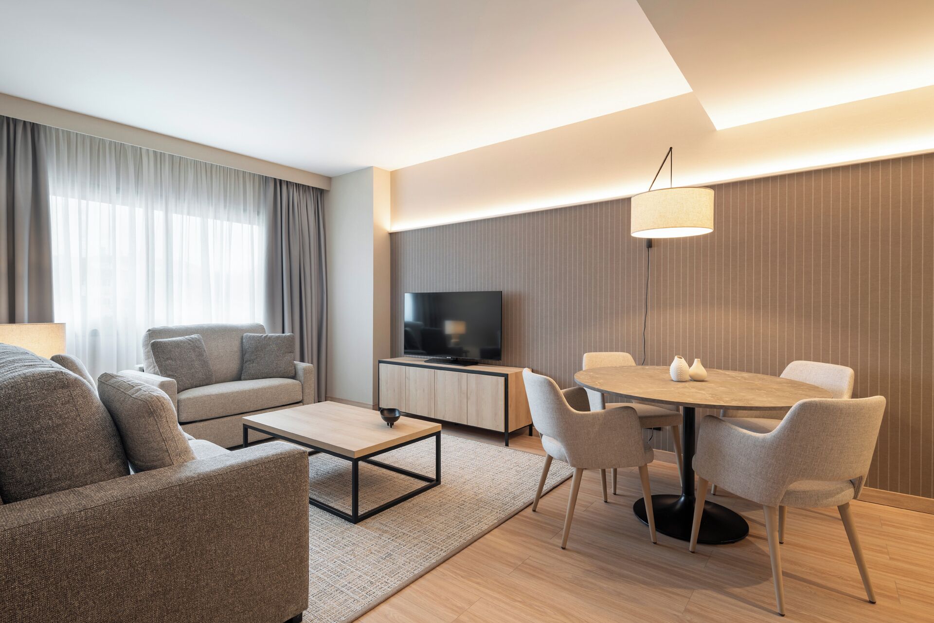 Una sala de estar moderna con un sofá, una mesa de centro, un televisor y un comedor con sillas y una mesa.