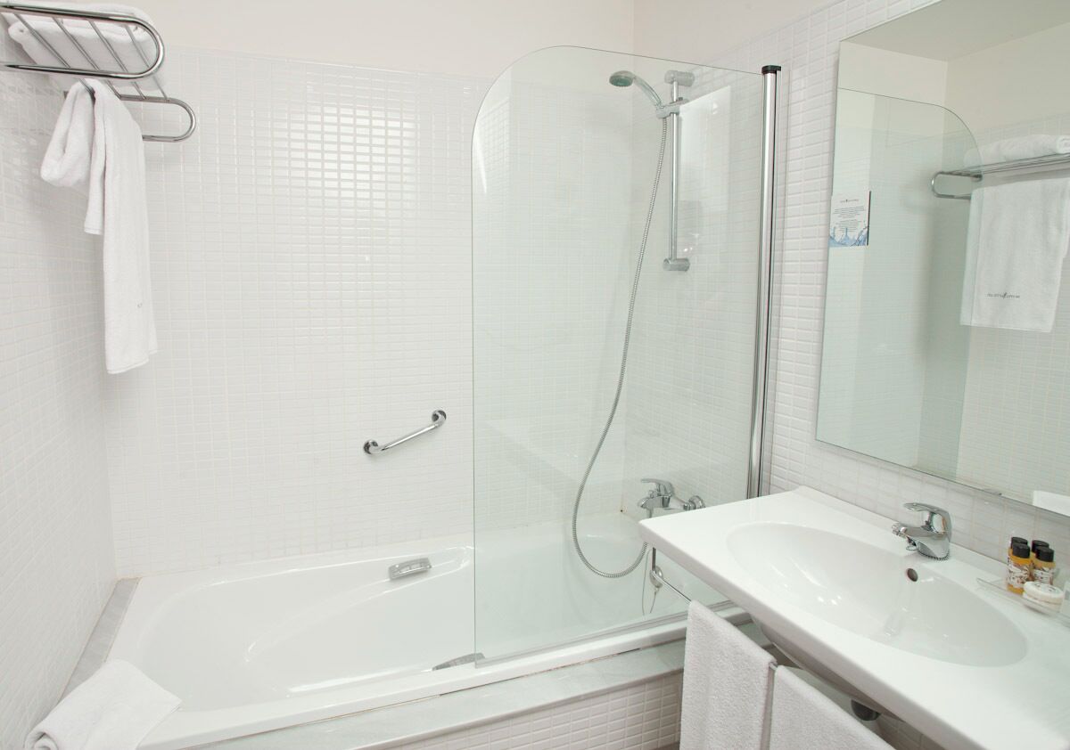 A modern bathroom with a glass-enclosed shower, a white bathtub, and a sink with a mirror.