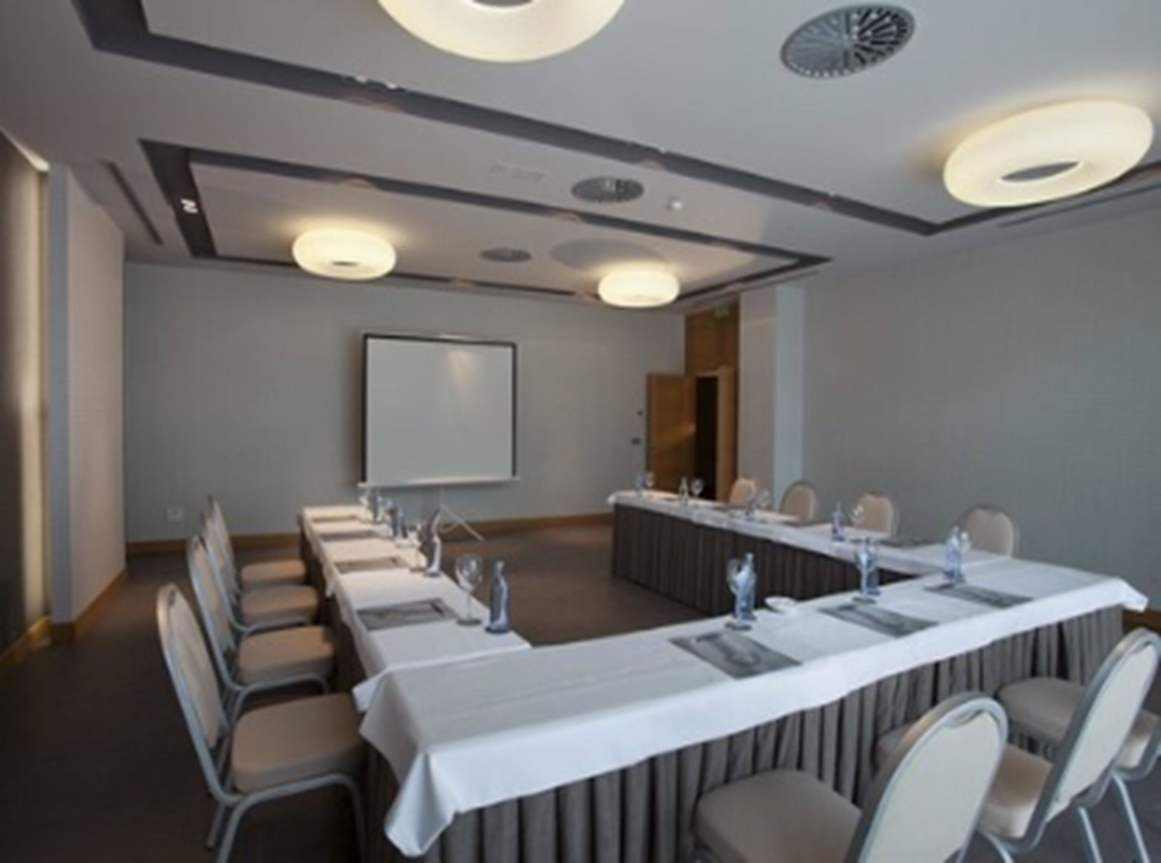 Un salón de conferencias con una larga mesa, sillas, una pantalla de proyector y una pizarra.