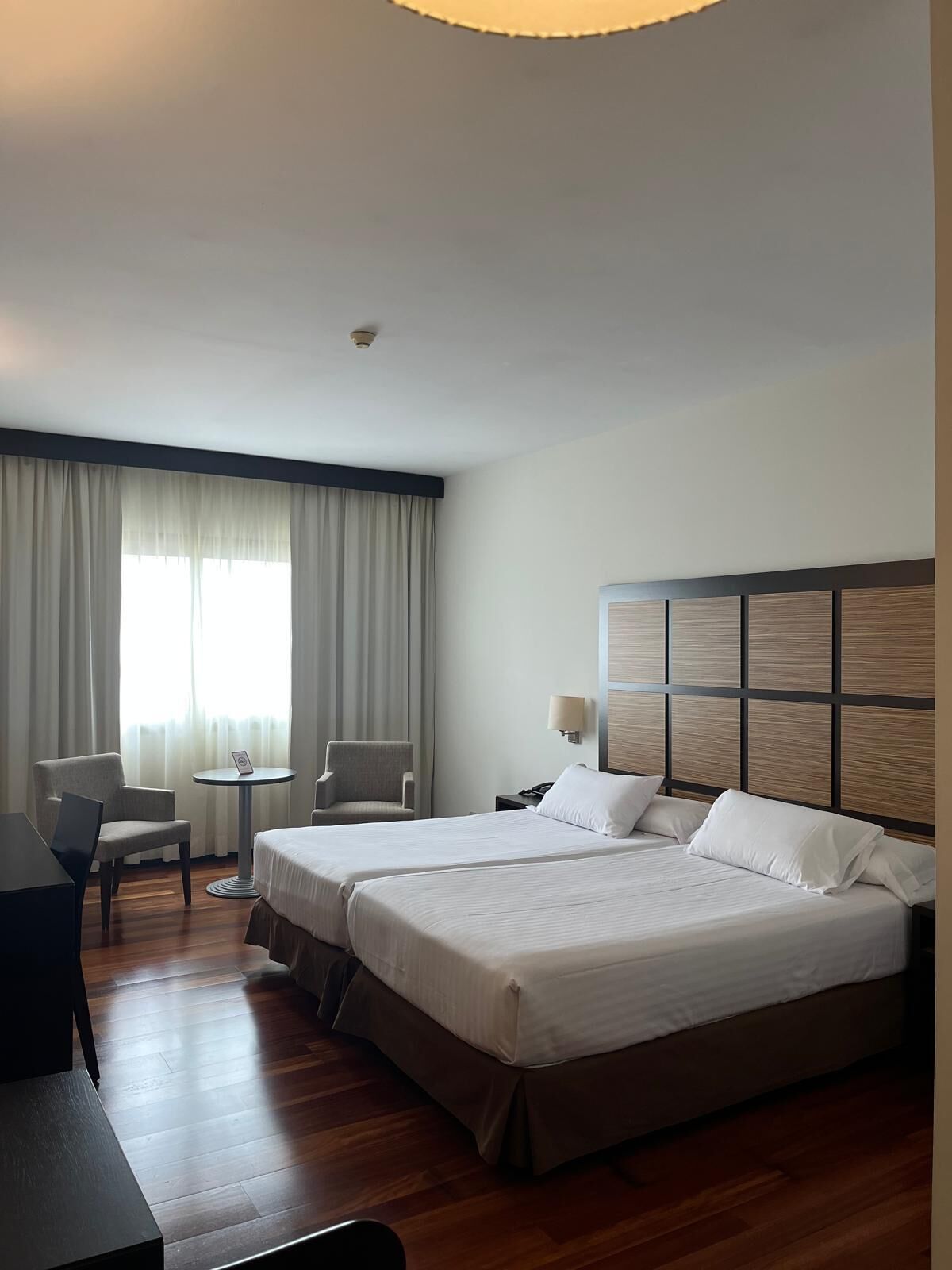 A hotel room with two beds, a desk, a chair, and a window with curtains.