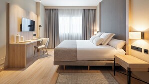 Una habitación de hotel moderna con una cama grande, un escritorio con silla, un televisor de pantalla plana y una mesita de noche con lámparas.
